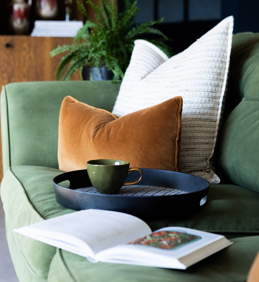 Cosy green bespoke upholstered velvet sofa with bespoke made soft furnishings, green mug on a coffee tray and an open book