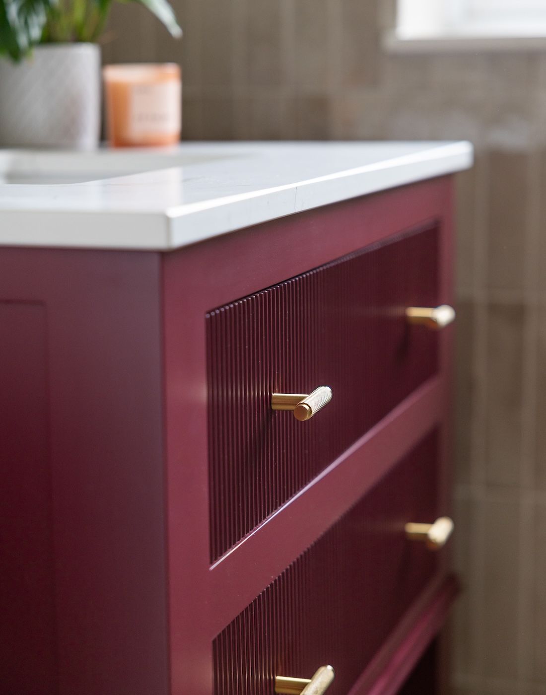 Art Deco Inspired Guest Bathroom/ Downstairs WC designed by Pfeiffer Design. Textured wallpaper in pale pink with half height tiling below, deep burgundy vanity unit with gold accent handles, warm wall lighting in a guest downstairs bathroom WC