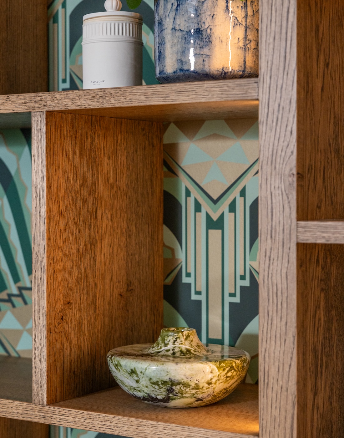 Art Deco Inspired Bespoke Bar and Library made by our bespoke joiners, designed by Pfeiffer Design. Art deco wallpapered insert within light timber open cabinetry, hints of gold through the backing and handles, and LED lighting for a warm but subtle glow