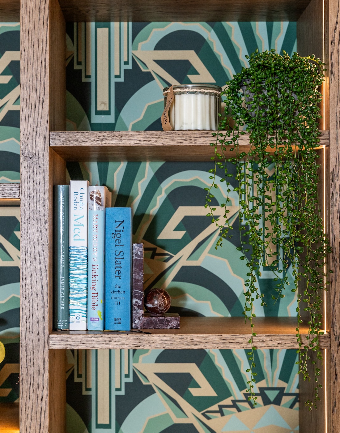 Art Deco Inspired Bespoke Bar and Library made by our bespoke joiners, designed by Pfeiffer Design. Art deco wallpapered insert within light timber open cabinetry, hints of gold through the backing and handles, and LED lighting for a warm but subtle glow