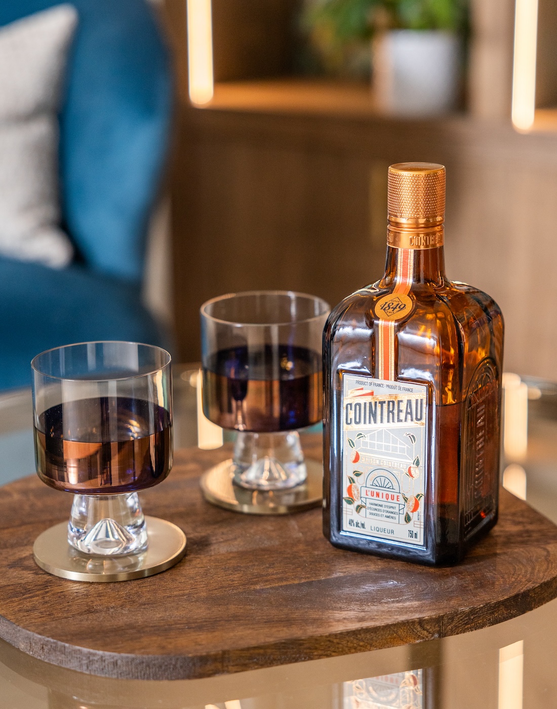 Art Deco Inspired Bespoke Bar and Library made by our bespoke joiners, designed by Pfeiffer Design. Foreground is bottle of drink and beautiful bronze glasses. Background is an art deco inspired joinery piece with LED lighting for a warm but subtle glow