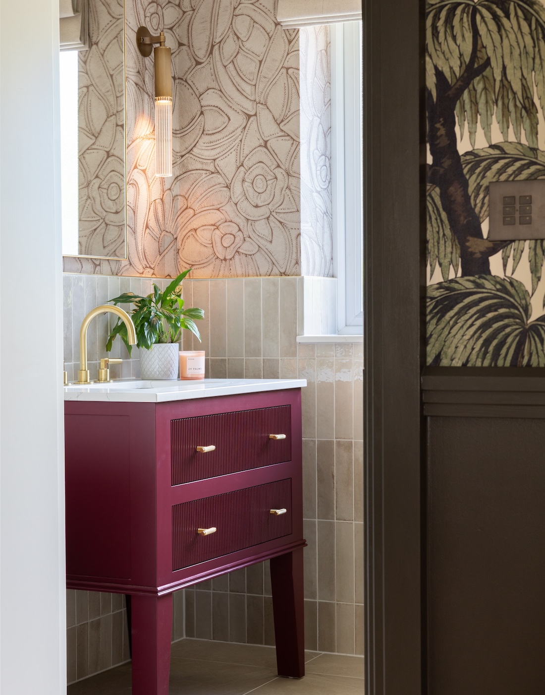 Art Deco Inspired Guest Bathroom/ Downstairs WC designed by Pfeiffer Design. Textured wallpaper in pale pink with half height tiling below, deep burgundy vanity unit with gold accent handles, warm wall lighting in a guest downstairs bathroom WC