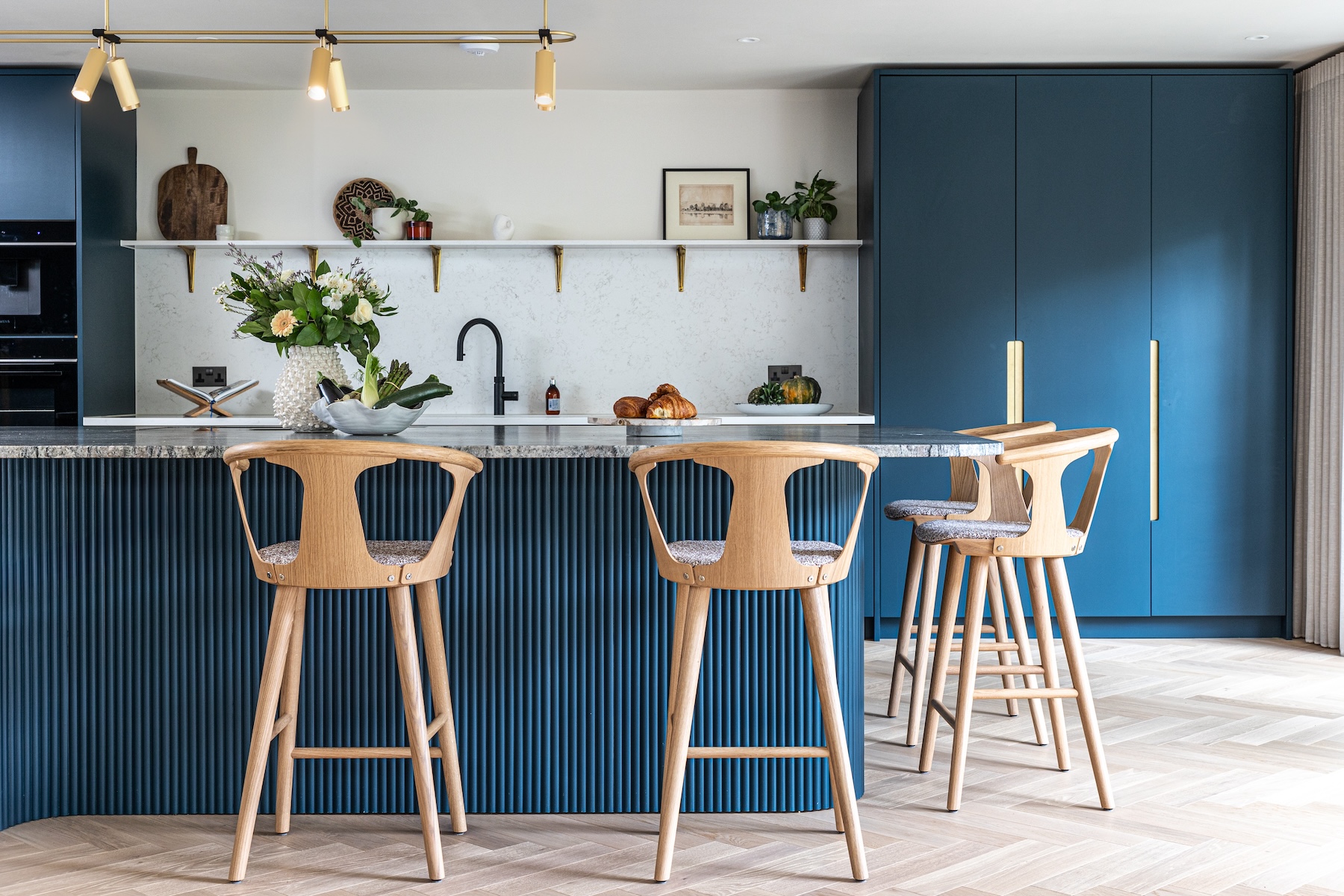 Art Deco Inspired Bespoke Kitchen made by our bespoke joiners, designed by Pfeiffer Design. Blue fluted timber island, breakfast cabinet, insert handles, light timber chevron flooring with timber bar stools